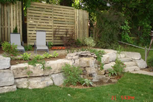 After: raised beds with stone retaining wall and pondless waterfall below sitting area with plantings