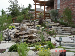 After: stone slab steps, waterfall and pond with wood archway, fence, lighting and plants